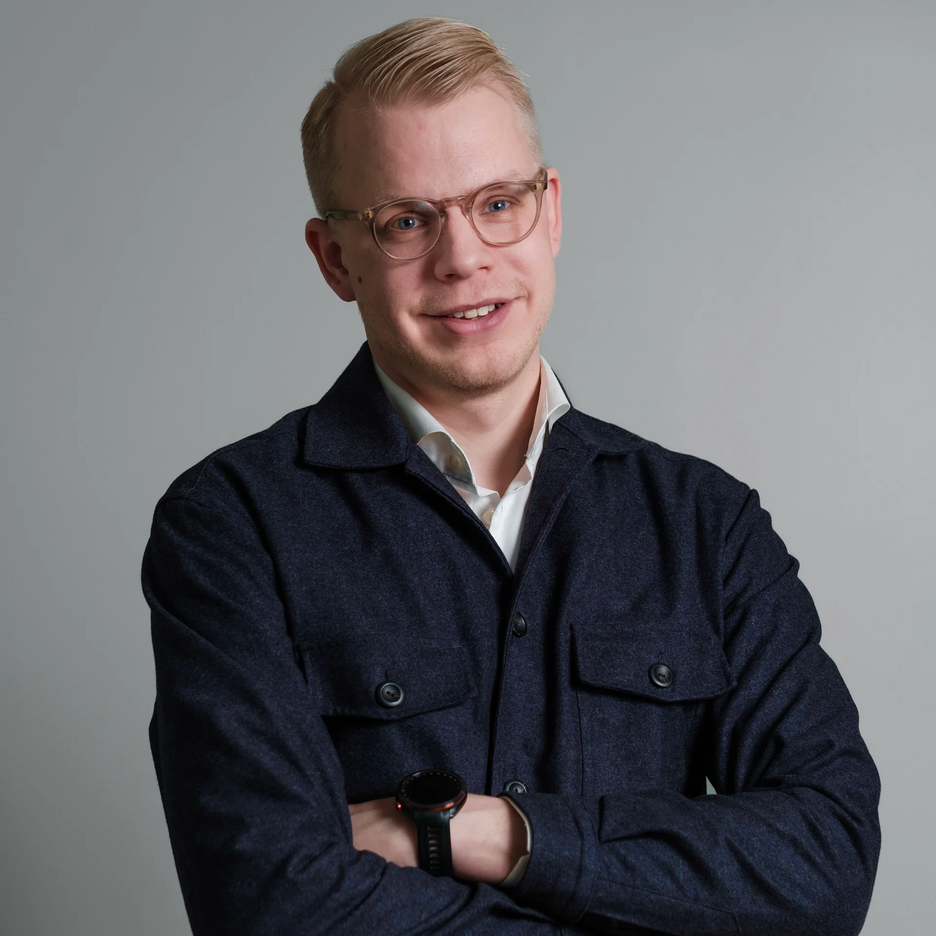En ung blond man med glasögon och korslagda armar ler mot kameran.